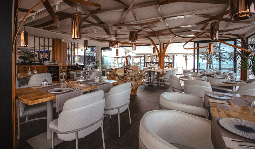 Elegant restaurant met tafels die op Tenerife zijn klaargemaakt, uitzicht op de buitenkant met palmbomen.