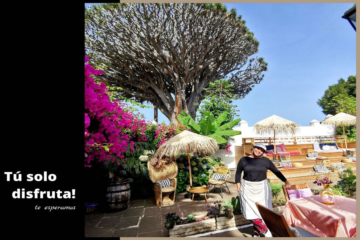 Patio met begroeiing, stroen parasols en één persoon op Tenerife. Tekst: Geniet er gewoon van! We wachten op je.