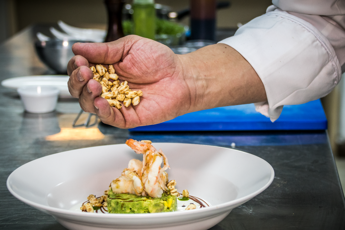 Chef's hand die granen toevoegt aan een gerecht met garnalen en avocado op Tenerife.