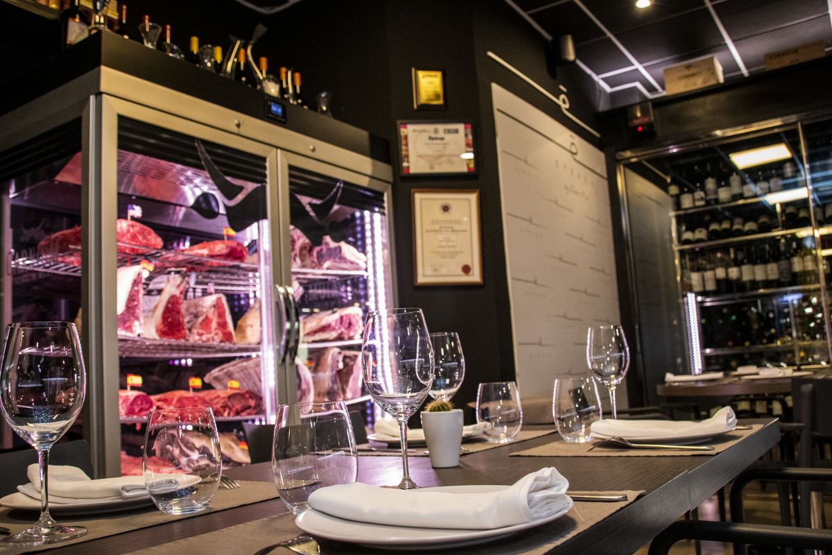 Tafel met wijnglazen, gevouwen servetten en koelkast met vlees in een restaurant op Tenerife.