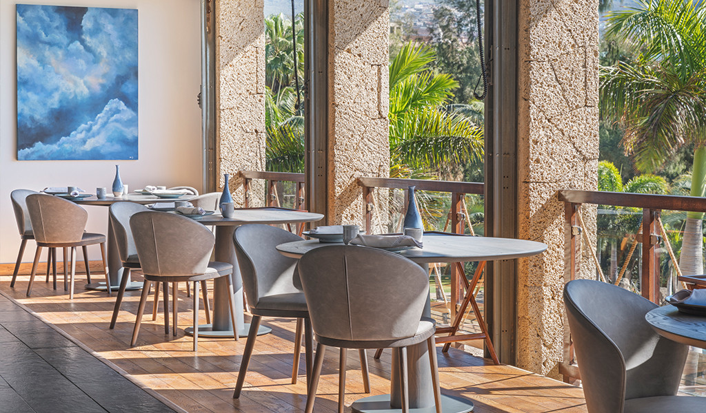 Eetzaal met tafels en stoelen naast grote ramen met uitzicht op de tuinen op Tenerife.
