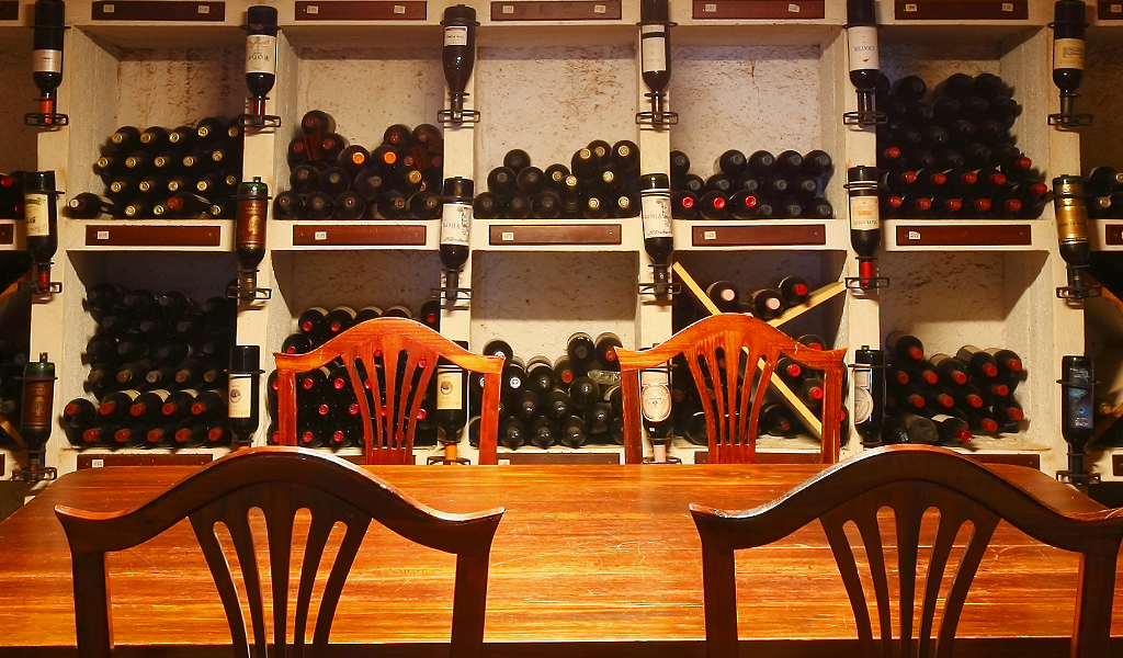 Houten tafel en stoelen voor een plank vol flessen wijn op Tenerife.
