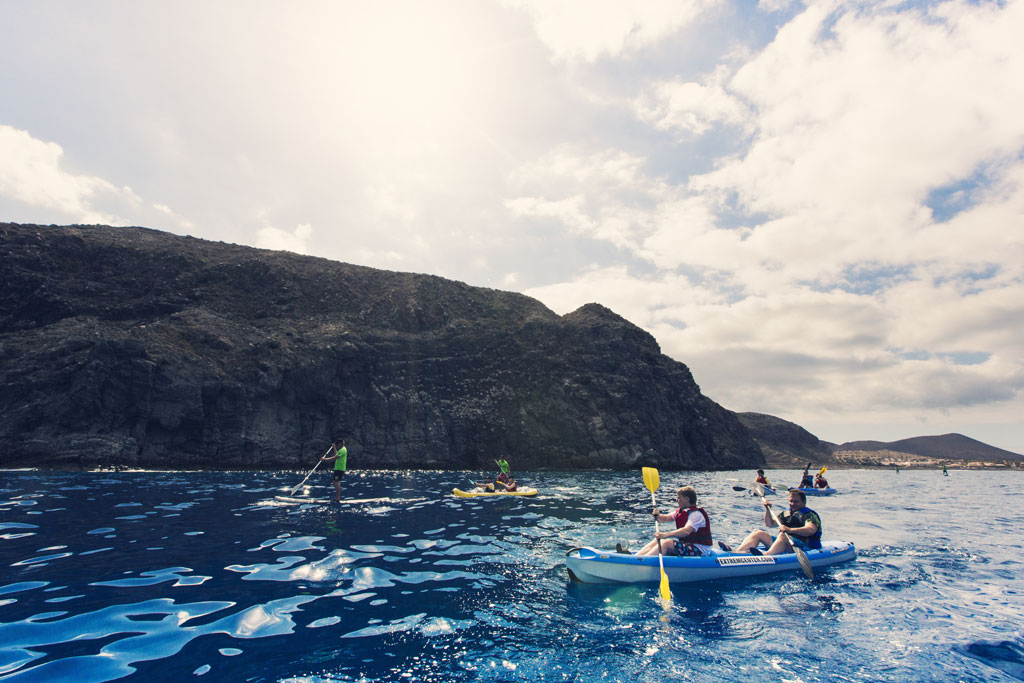 Mensen die kajakken en peddelen surfen aan de kust van Tenerife met bergen op de achtergrond.
