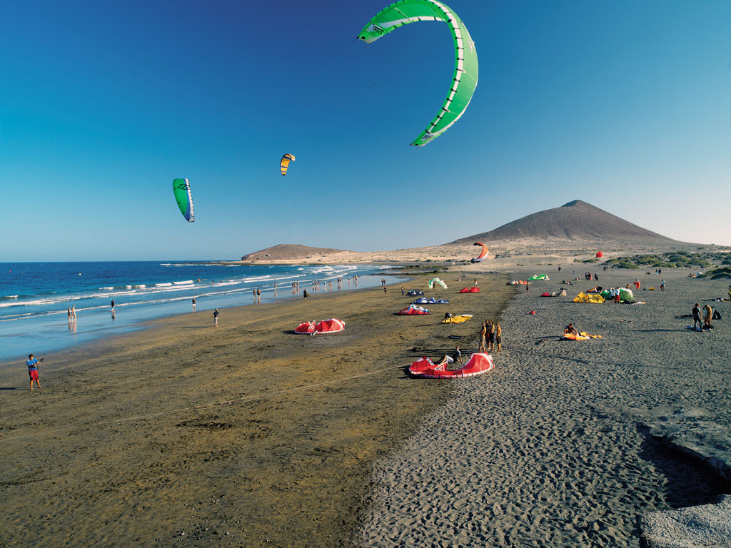 Mensen die kitesurfen op het strand van El Médano, Tenerife, met bergen op de achtergrond.
