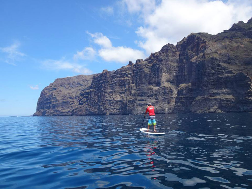 Persoon peddelt surfen voor de kliffen van Los Gigantes, Tenerife.