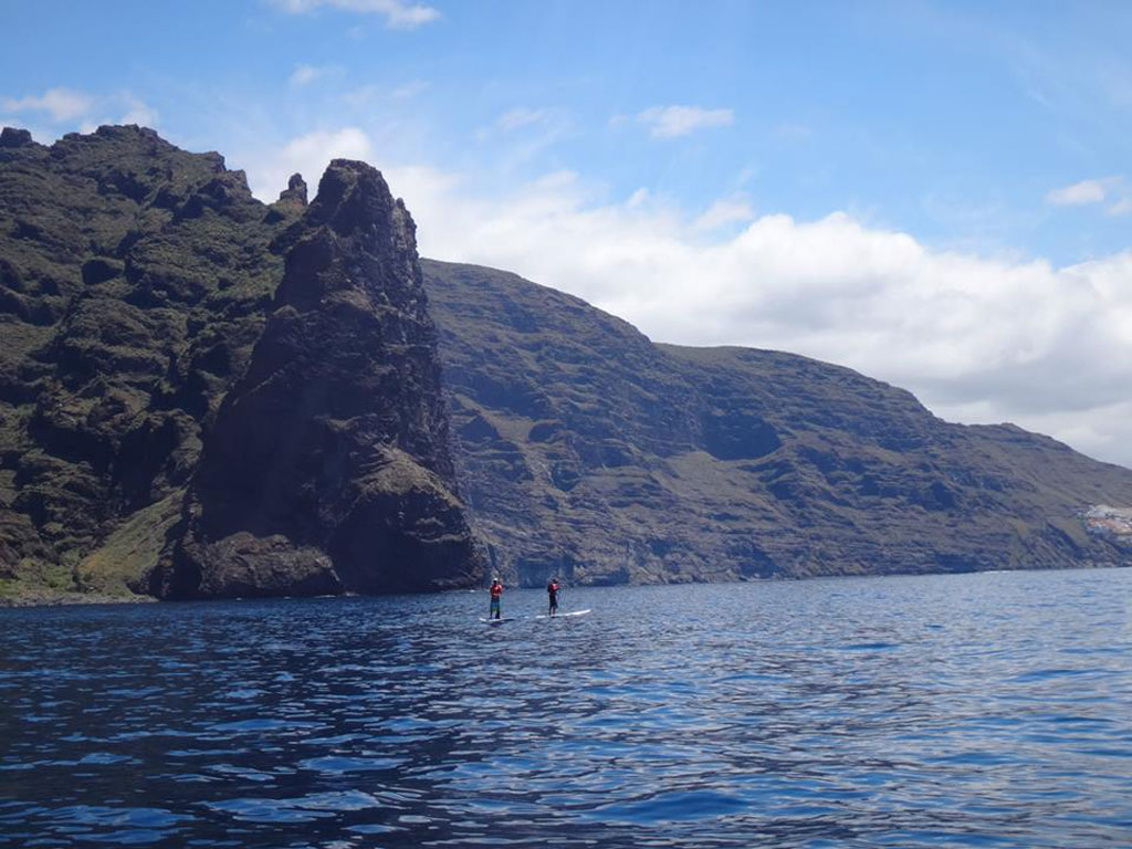 Mensen peddelen surfen voor de kliffen van Los Gigantes, Tenerife.