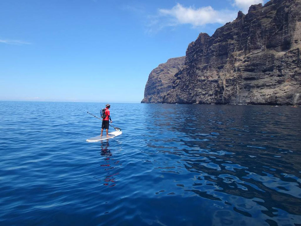 Persoon peddelt surfen voor de kliffen van Los Gigantes, Tenerife.