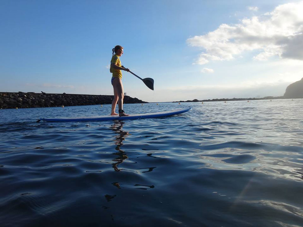 Persoon die bij zonsondergang aan de kust van Tenerife paddlesurft.