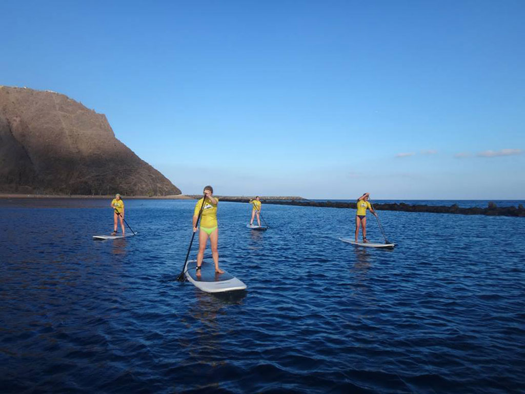 Mensen peddelen surfen naast een rots in Las Gaviotas, Tenerife.