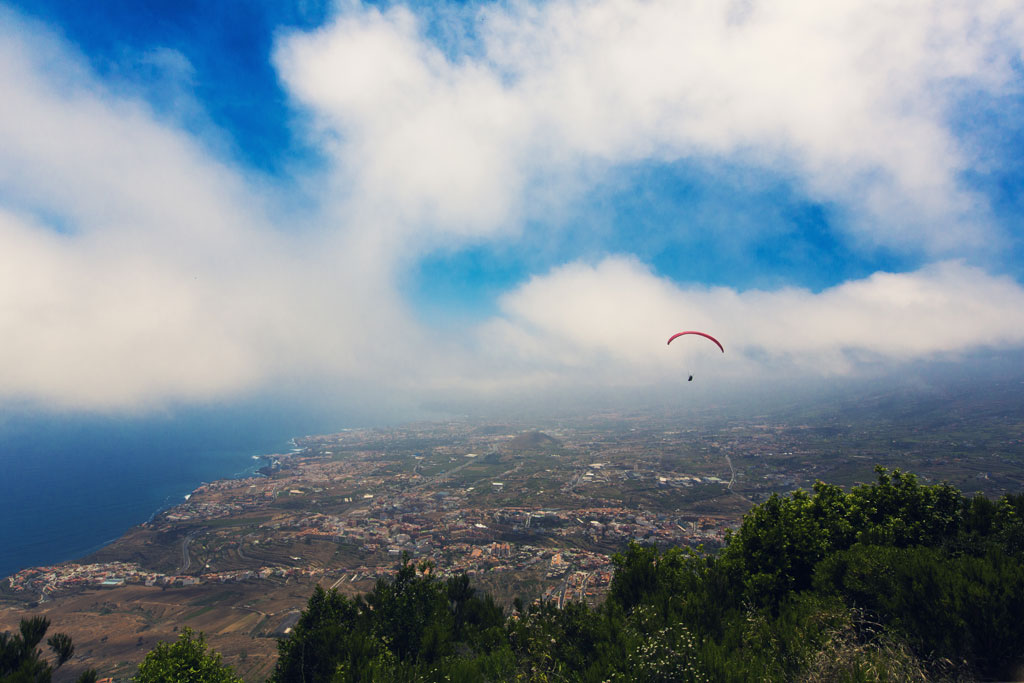 Paragliding vliegen over het kustlandschap van Tenerife onder een deels bewolkte lucht.