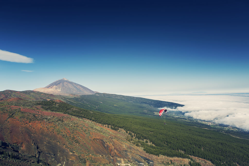 Paragliden boven de berg Teide op Tenerife, met wolken en vulkanisch landschap.