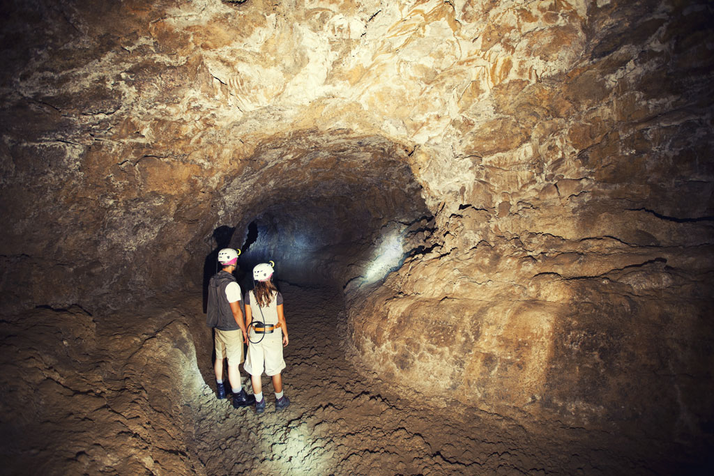 Ontdekkingsreizigers met helmen lopen door een tunnel in Cueva del Viento, Tenerife.