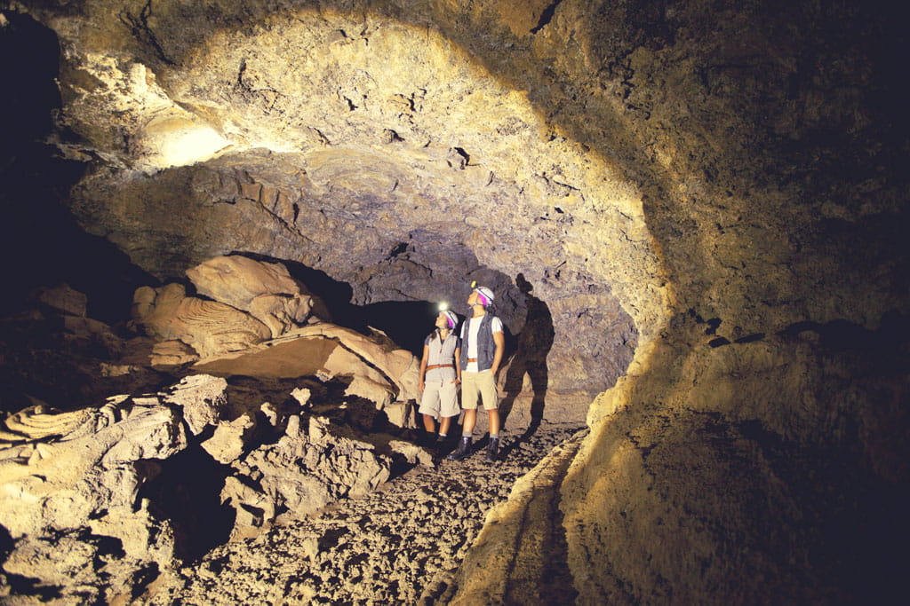 Mensen die vulkanische groten op Tenerife verkennen met helmen en zaklampen.