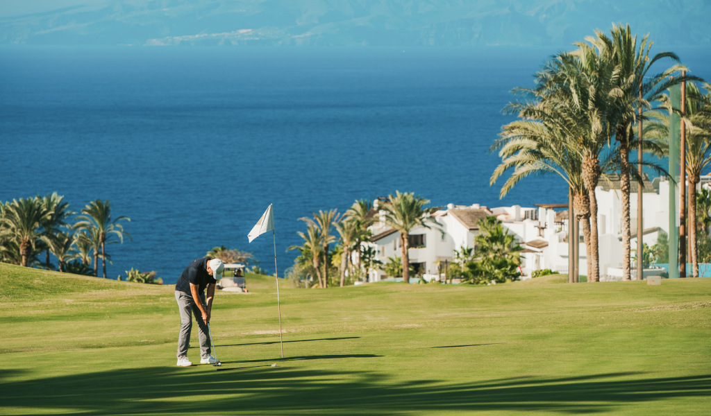 Iemand die golf speelt op een baan met uitzicht op zee en huizen op Tenerife.