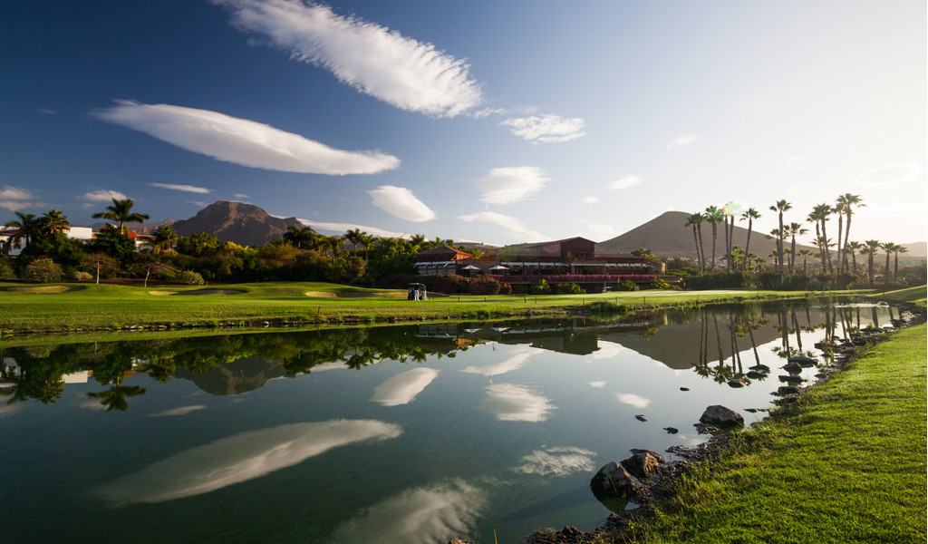 Golfbaan met bergen en palmbomen die weerspiegeld zijn in een meer op Tenerife.