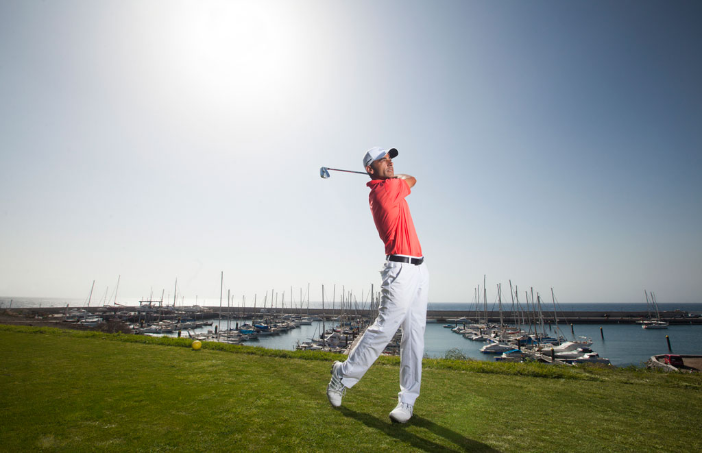 Golfer tijdens een swing met de jachthaven en boten op de achtergrond op Tenerife.