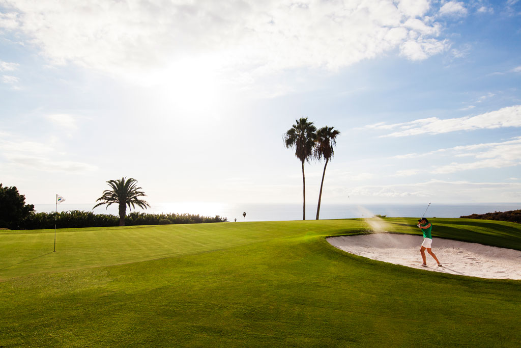 Iemand die golf speelt op een zeebaan op Tenerife met palmbomen en heldere luchten.