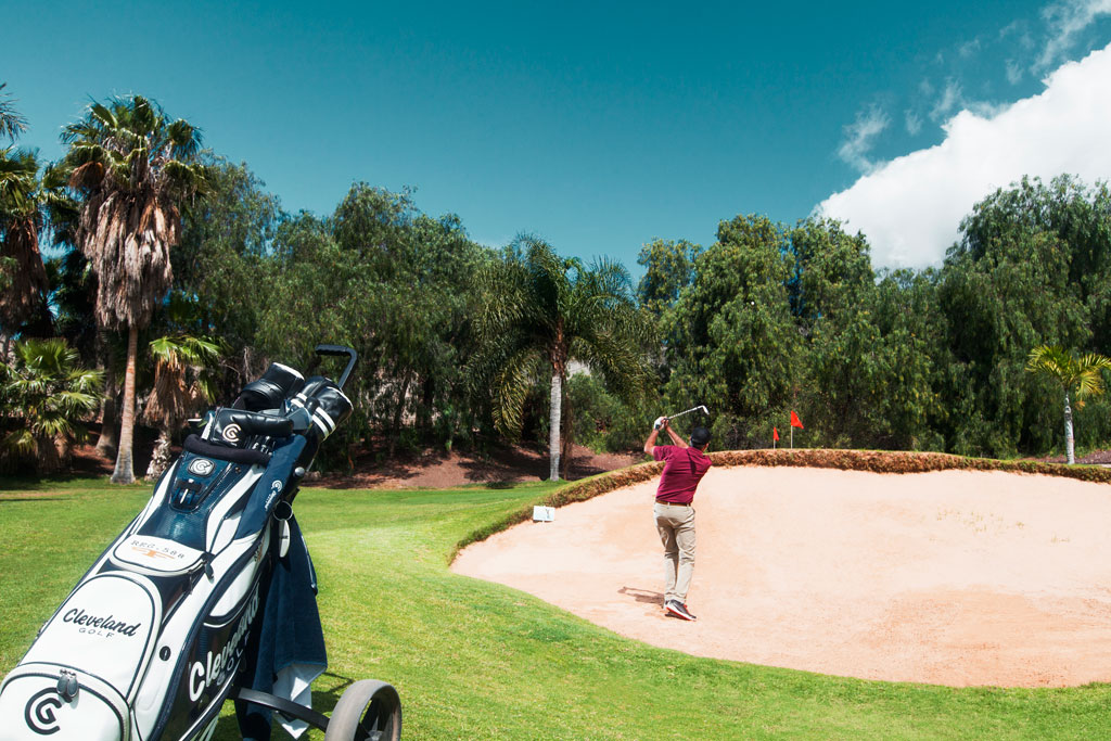 Golfer in actie op een baan op Tenerife, vlakbij een bunker.