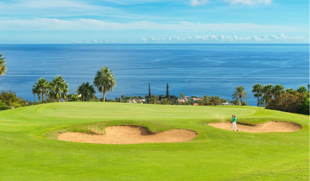 Golfbaan op Tenerife met uitzicht op zee. Slagen bij bunkers omringd door palmbomen.