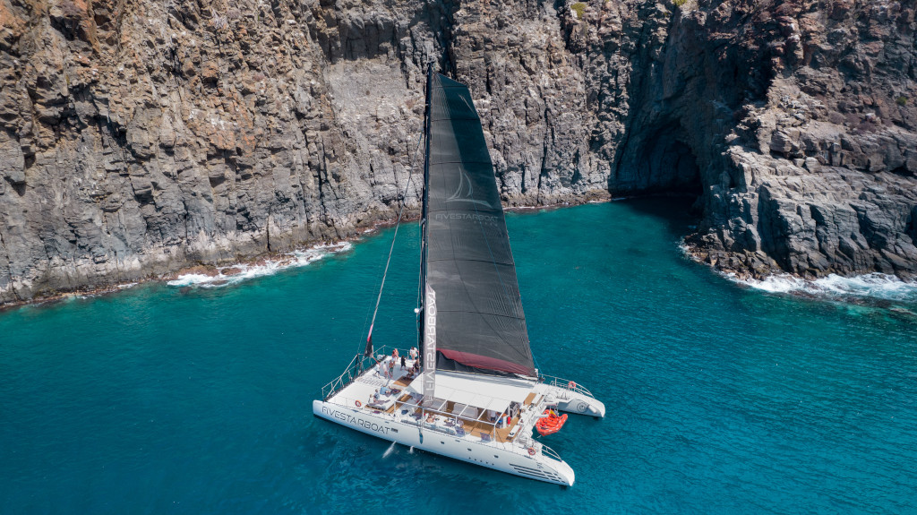 Catamaran die zeilt bij rotsachtige kliffen aan de kust van Tenerife.