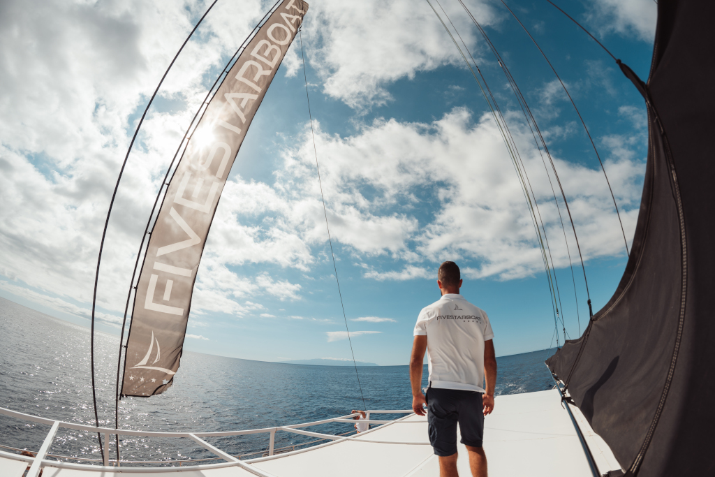 Persoon op de boeg van een boot met een T-shirt waarop FIVESTARBOAT staat, uitkijkend over zee op Tenerife.