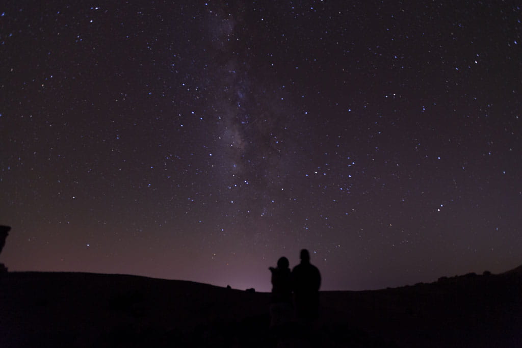 Sterrenhemel boven de berg Teide op Tenerife met twee silhouetten die toekijken.