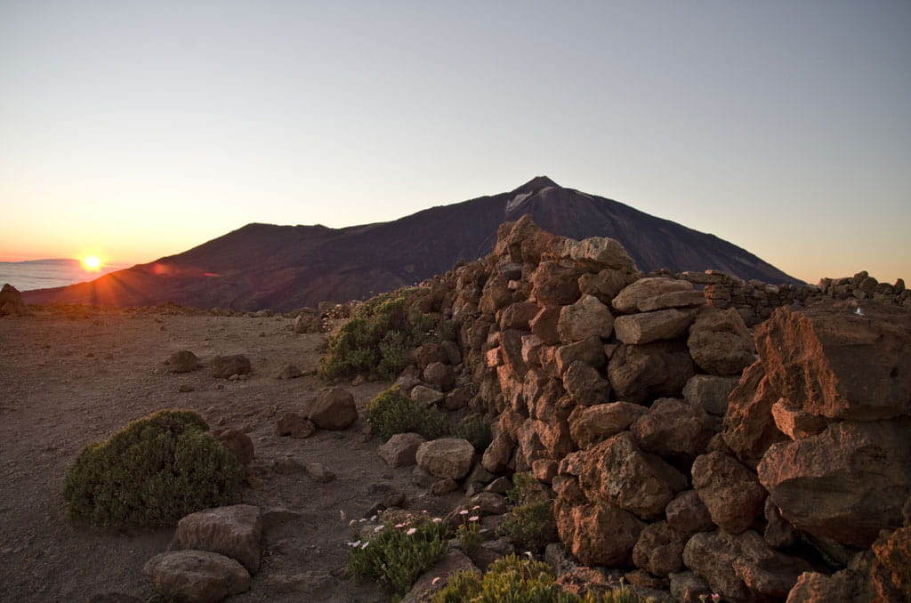 Zonsopgang op El Teide, Tenerife, met rotsen en vegetatie op de voorgrond.