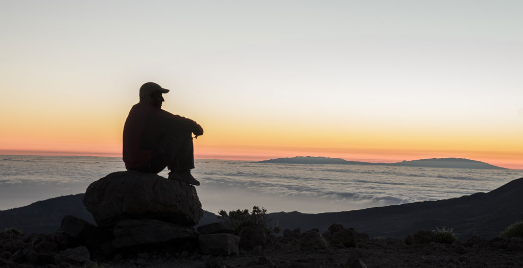 Iemand die op een rots zit en naar de zonsondergang op Tenerife kijkt.