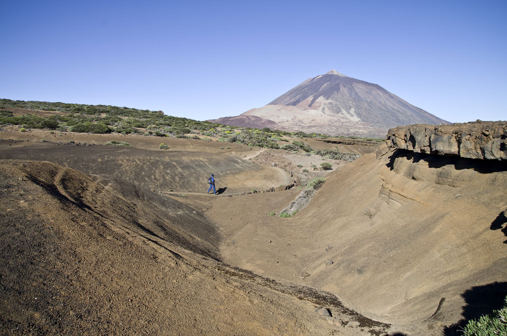 Persoon die bij de Teide-vulkaan op Tenerife loopt onder een heldere lucht.