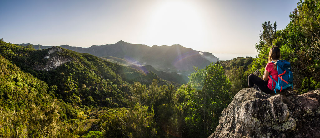 Iemand met een rugzak die bij zonsondergang naar het bergachtige landschap op Tenerife kijkt.