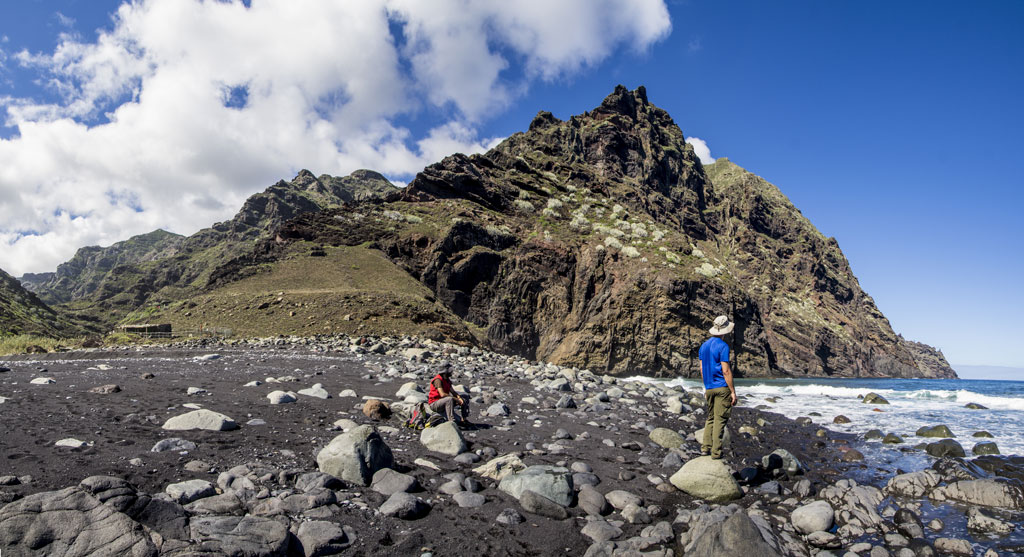 Mensen op een zwart zandstrand met bergen aan de kust van Tenerife.