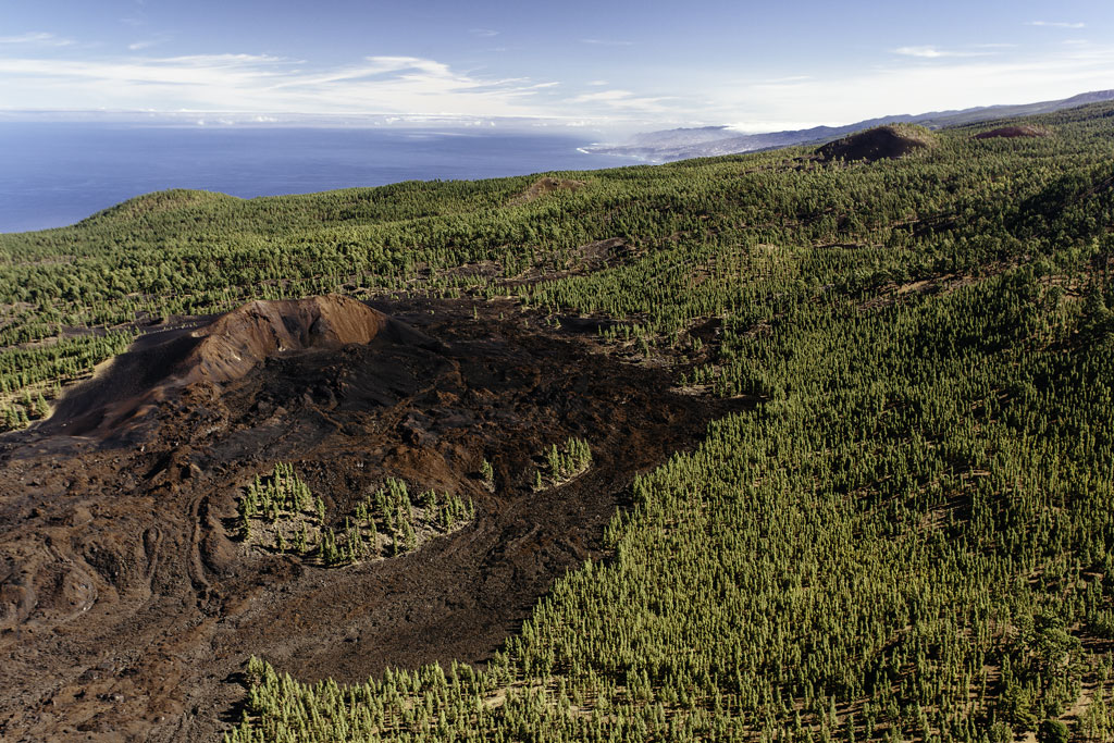Vulkanische krater omgeven door bos in La Palma, Tenerife, met de zee op de achtergrond.
