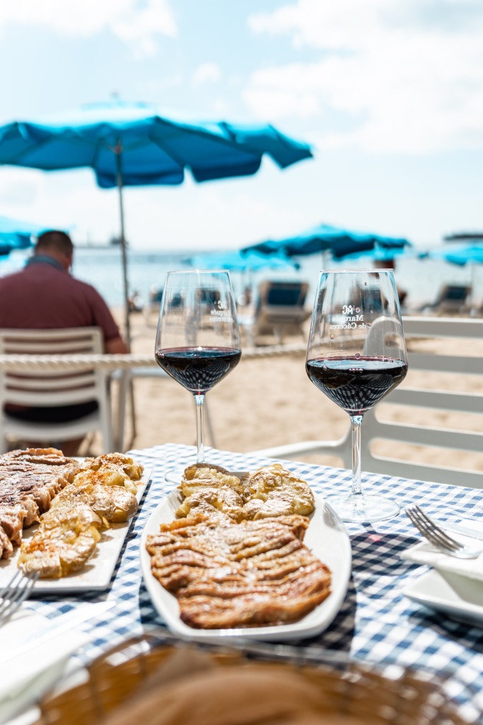 Glasen wijn en eten op het strand met blauwe parasols op Tenerife.