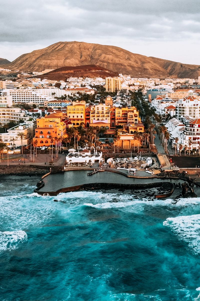Luchtfoto van de kust van Tenerife met gebouwen en een berg op de achtergrond.