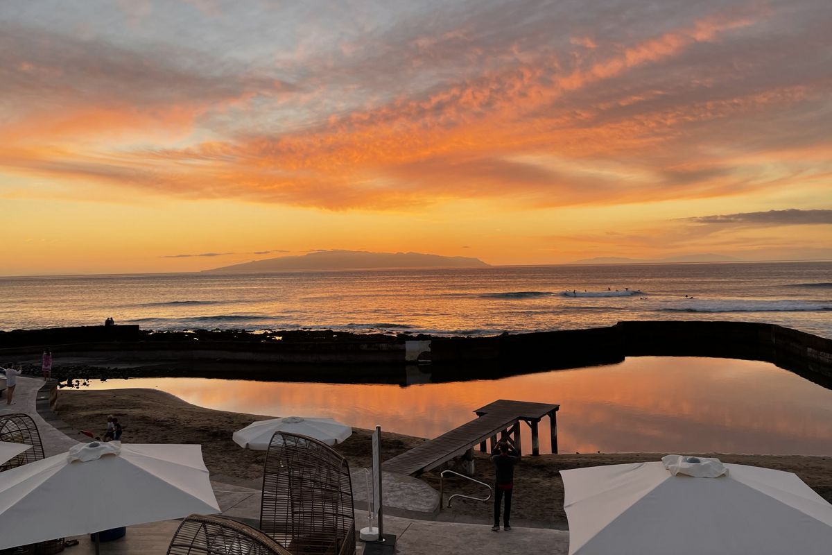 Zonsondergang boven de oceaan op Tenerife met oranje luchten en parasols op de voorgrond.
