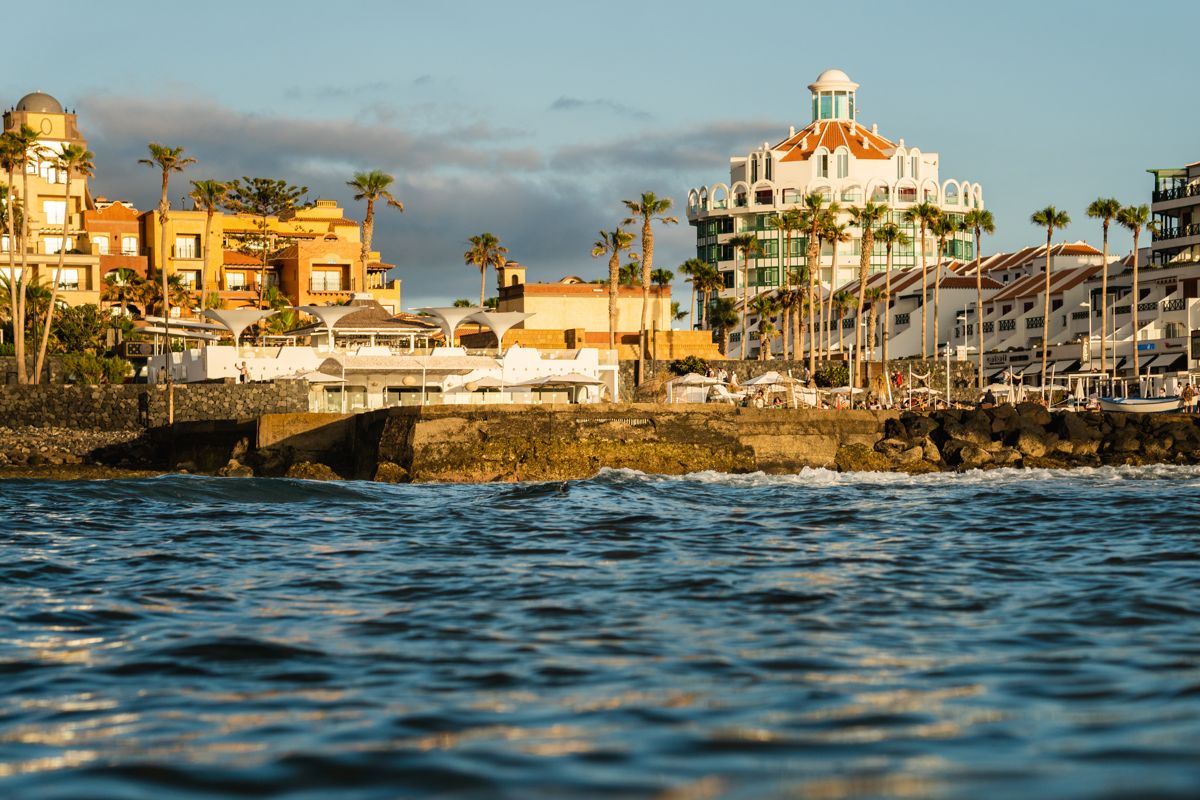 Uitzicht op de kust van Tenerife bij zonsondergang met gebouwen en palmbomen.