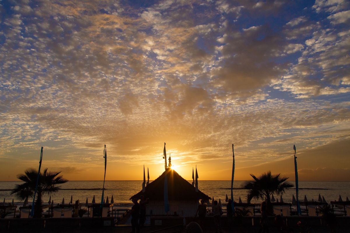 Zonsondergang op het strand met parasols en palmbomen op Tenerife.