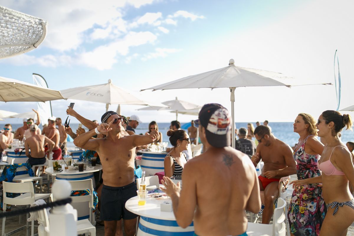 Mensen die genieten van een strandfeest op Tenerife, met parasols en tafels.
