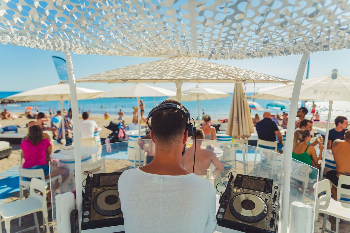 DJ die muziek speelt op een strand op Tenerife met mensen die genieten van de zee.