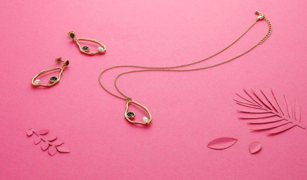 Gouden ketting en oorbellen met parels op een roze achtergrond en bladversieringen.