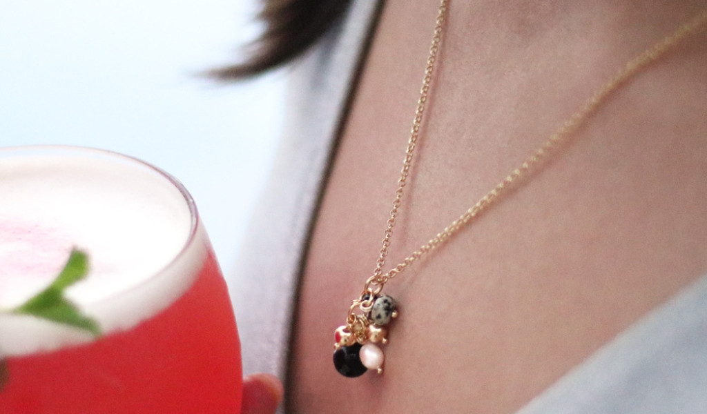Ketting met hangers en roze drankje in een glas met een persoon.