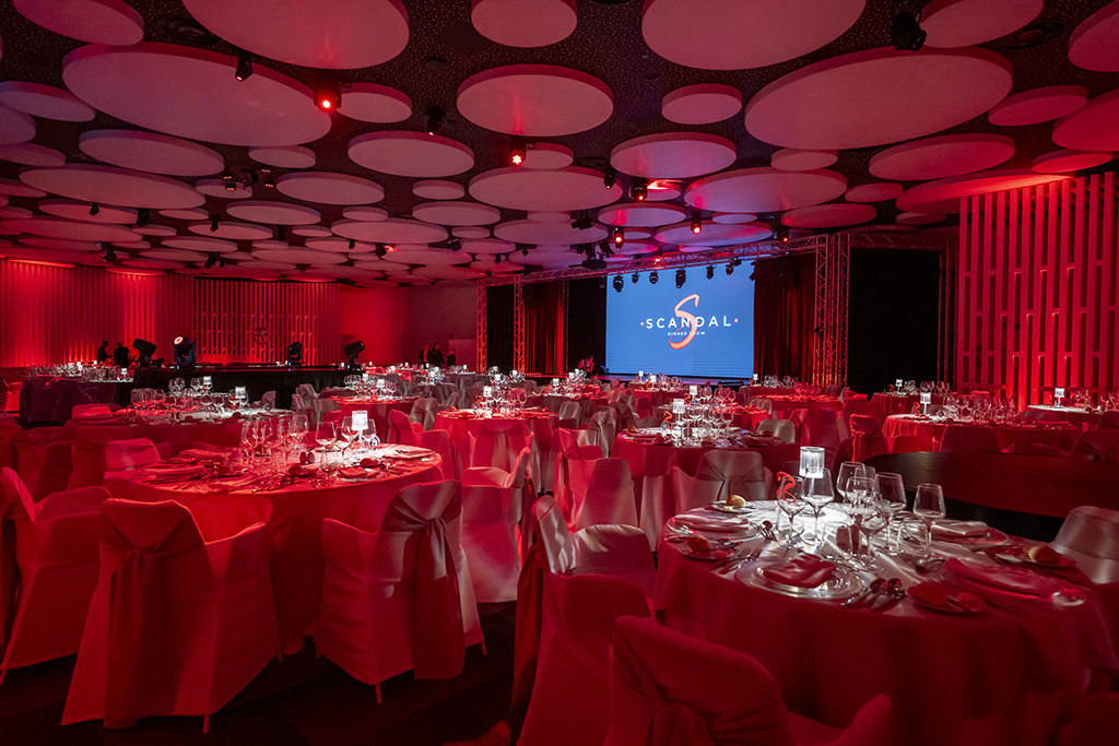 Evenementenruimte met versierde tafels en scherm met het logo van SCANDAL Show Tenerife.