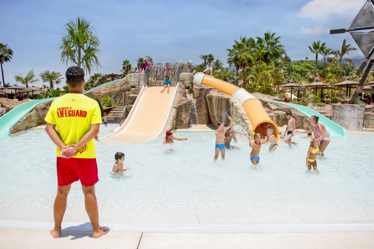 Strandwacht die kinderen kijkt die op glijbanen spelen in het waterpark op Tenerife.