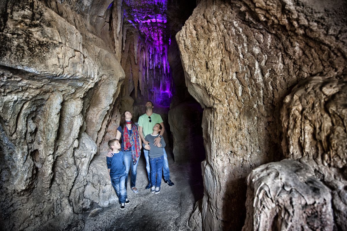 Familie die een grot op Tenerife verkent, paarse verlichting die het interieur benadrukt.