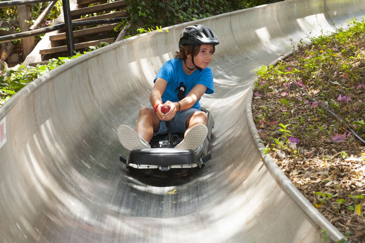 Jongen met zwarte helm die glijdt op een gebogen metalen glijbaan op Tenerife.