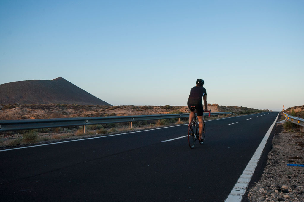 Fietser op de weg bij een vulkaan op Tenerife bij zonsondergang.