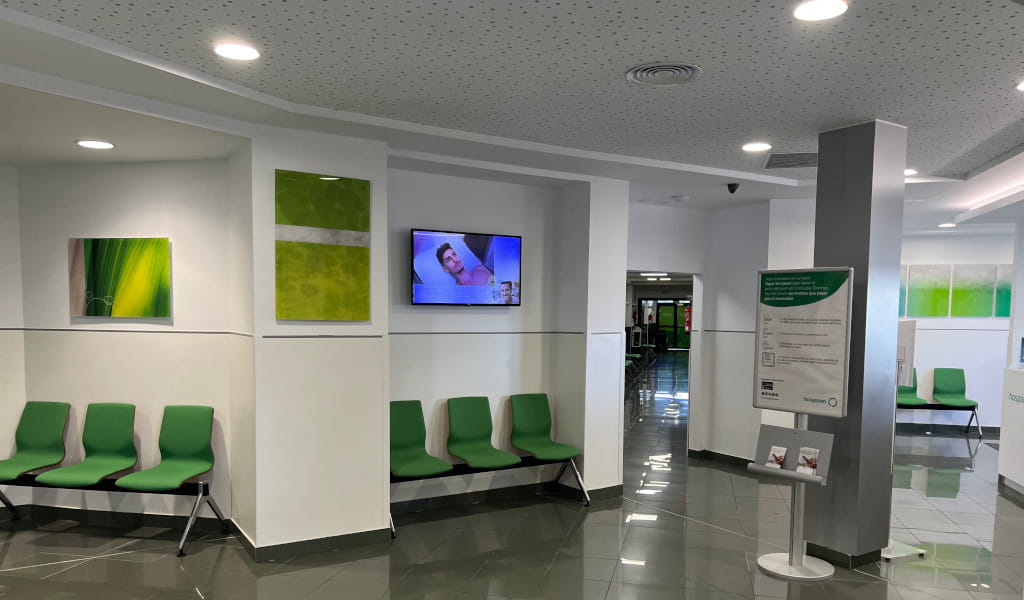 Wachtruimte met groene stoelen en verlichte schermen in een kliniek op Tenerife.