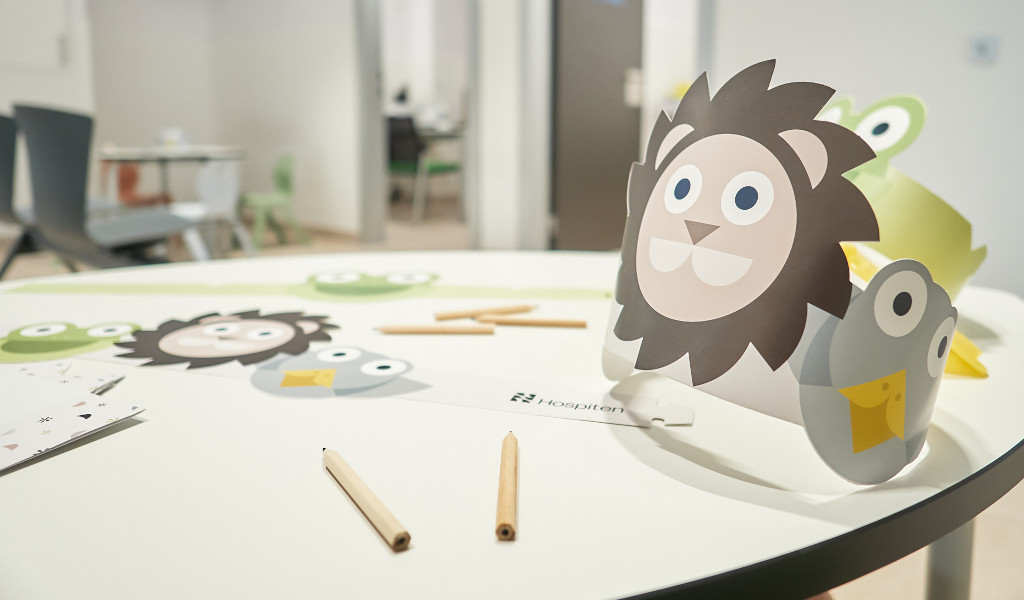 Tafel met knutselmaterialen voor kinderen in een ziekenhuis op Tenerife, waaronder papieren kransen met dierenontwerpen.