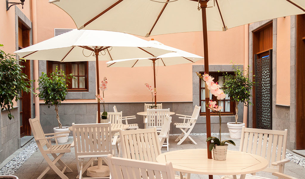 Terras met witte tafels en stoelen onder parasols in een binnenplaats op Tenerife.