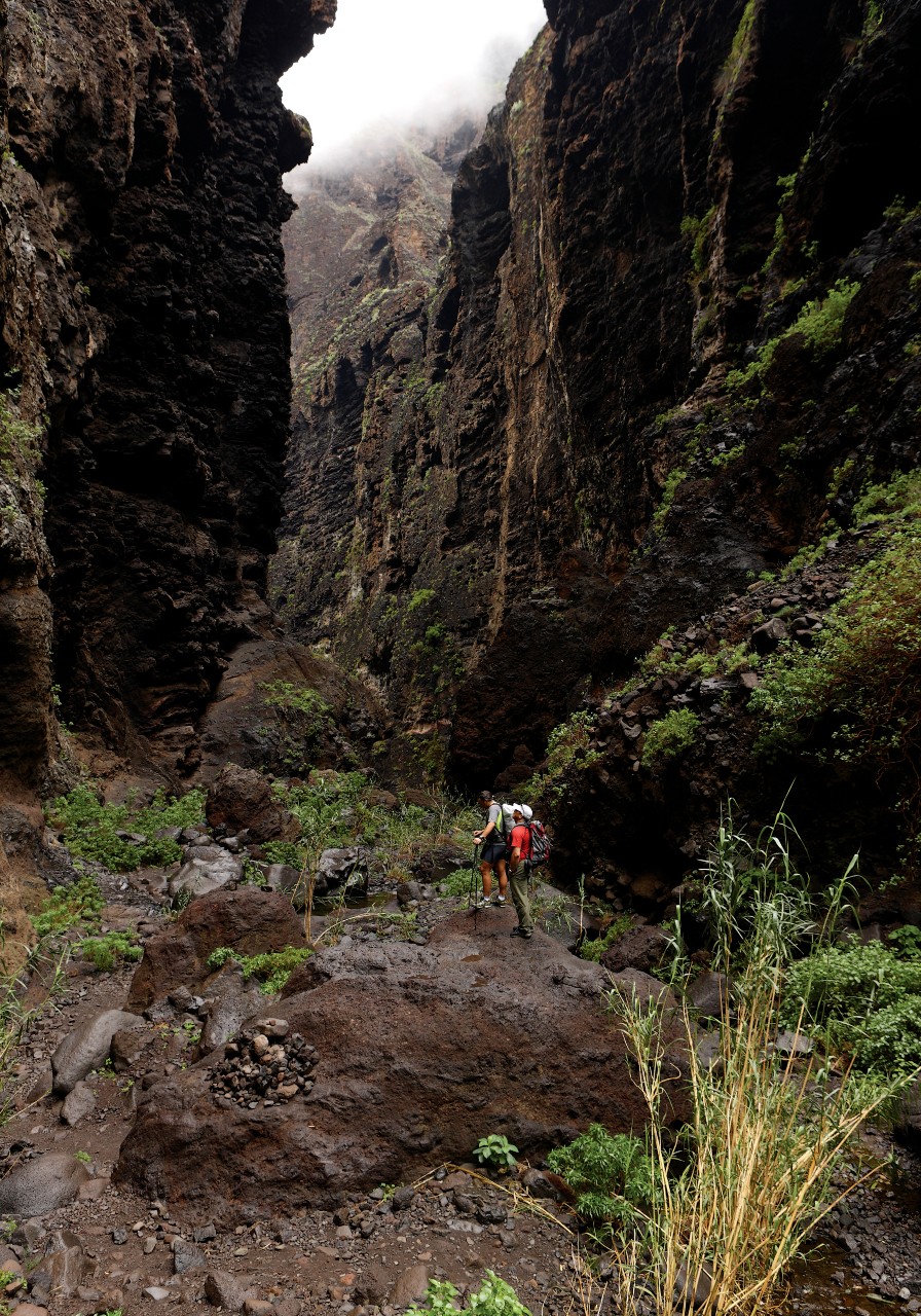 Twee mensen lopen door de Barranco de Masca op Tenerife, omringd door hoge rotswanden.